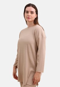 Beige ribbet langærmet top med rund halshals, der har en afslappet pasform og sideskår for nem bevægelse. Blød tekstur.