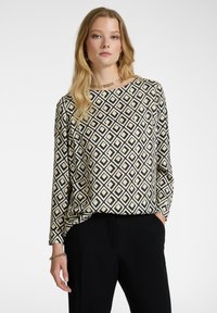 Långärmad topp med ett svart och vitt diamantmönster med gula accenter. Mjuk tyg och avslappnad passform; rund halsringning. Matchas med svarta byxor.