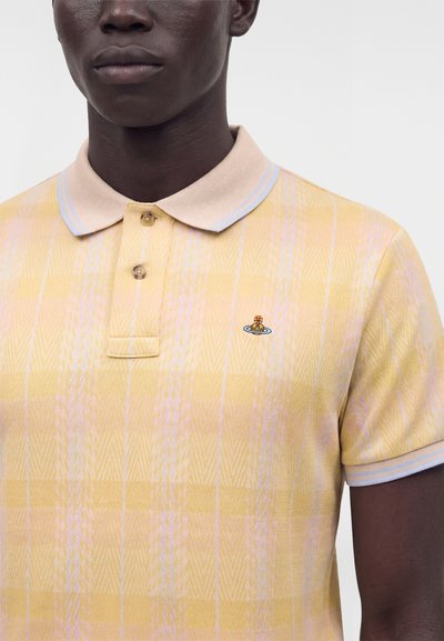 Homme portant un polo jaune et rose à motifs avec un col beige et un petit logo brodé sur la poitrine gauche.