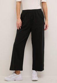 Black wide-leg pants with an elastic waistband, made of lightweight fabric. Worn with white sneakers, featuring a relaxed fit and minimal design.