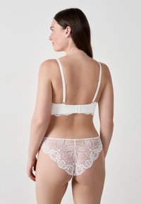 Bralette en dentelle blanche et thong assorti, avec des bords festonnés, de fines bretelles et des motifs floraux complexes au dos.