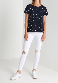 Marineblauw polka dot T-shirt met korte mouwen, gecombineerd met witte skinny jeans met scheuren en witte sneakers. Gladde stof met een ontspannen pasvorm.