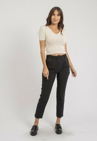 Haut blanc côtelé à manches courtes avec un col en V, associé à un pantalon noir ajusté avec une ceinture à boucle ronde. Chaussures noires brillantes.