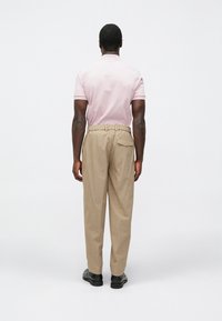 Polo cor-de-rosa com acabamento branco, combinado com calças largas bege com cós elástico e bolso na parte de trás. Sapatos pretos.