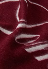 Tissu en laine bordeaux avec une texture douce et floue, présentant des motifs abstraits blancs tourbillonnant à la surface.