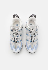 Pantofi sport gri deschis cu accente albastre, având un superior din plasă și material sintetic, design cu șireturi și talpă texturată cu un model ondulat.