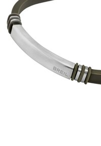 Breilarmband med en borstad silvermetallcenter, olivgrön silikonrem och spiralformade detaljer nära spännet för extra karaktär.