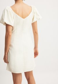 Vit linnklänning med puffärmar, djup V-back, figurnära bodice och lätt utsvängd kjol, som visar upp en minimalistisk design och mjuk textur.