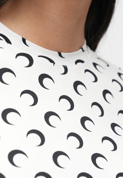 Tecido branco com textura suave e padrão repetido de luas crescentes pretas. Gola alta e design justo.