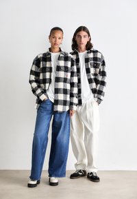 Sort-hvide ternede flannel skjorter med lommer; parret med blå brede bukser og hvide løse bukser. Chunky fodtøj synligt.
