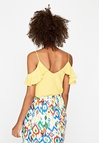 Top giallo senza spalline con maniche a volant, abbinato a una gonna a stampa multicolore con design ondulati in blu, rosso, verde e bianco.