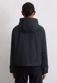 Ciemnoniebieska krótka kurtka z kapturem, o gładkiej fakturze i zapinanych mankietach. Detal na plecach prezentuje przeszycia oraz prosty design.