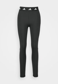 Leggings neri con un design aderente e vita elasticizzata, caratterizzati da un motivo a logo Adidas bianco ripetuto lungo la banda. Texture liscia.
