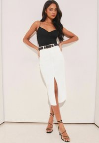 Fekete ujjatlan felső V-kivágással, magas derekú fehér szoknyával párosítva, elöl hasítékkal, fekete övvel és pántos magassarkú cipőkkel kiemelve.