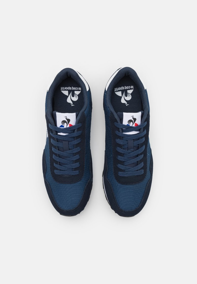 Zapatillas azul marino con parte superior de malla texturizada, cordones, cuello acolchado y detalles en blanco. Logo visible en la lengua y en el talón.