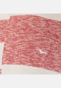 Tessuto a maglia a righe rosse e bianche con una consistenza morbida, caratterizzato da un piccolo dettaglio ricamato bianco.