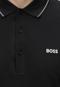 Sort polo-shirt med hvid kant på kraven, tre sorte knapper og hvidt "BOSS" logo broderet på brystet.