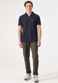 Marineblauwe poloshirt met een gestructureerde afwerking, korte mouwen en een subtiele logo. Gecombineerd met olijfgroene broek en grijze sneakers.
