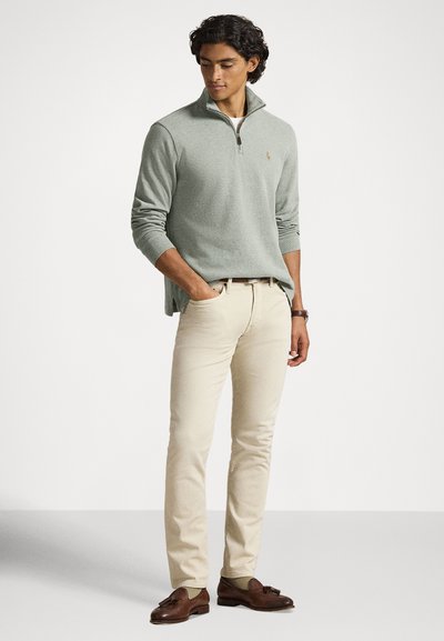 Light green, textured zip-up sweater, beige pants, and brown loafers. Sweater features a collar and small emblem on the chest.