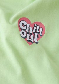 Tela de algodón verde claro con un gran diseño de corazón rosa y el texto "Chill Out" en letras negritas negras.