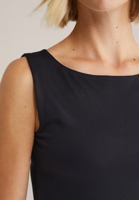 Musthave seljauseta must särk, millel on sile tekstuur ja avar kaelus. Lähedalt vaadates on nähtav kaeluse ja õlgade piirkond.