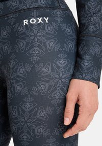 Czarne legginsy z białym wzorem śnieżynek i logo Roxy. Teksturowana tkanina o dopasowanym kroju, podkreślająca ścisły fason w okolicach talii i mankietów.