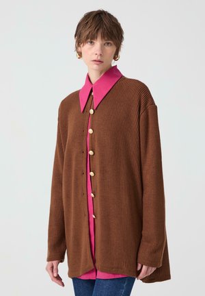 Bruine gebreide cardigan met een brede silhouet, voorzien van een roze kraagshirt eronder en gouden knopen aan de voorkant. Geweven stof, comfortabele pasvorm.