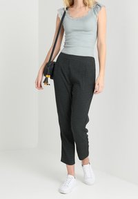 Jasnoniebieski prążkowany top na ramiączkach z koronkowym wykończeniem, w połączeniu z czarnymi spodniami w wzory i białymi trampkami, nosząc małą czarną torebkę na ramię.