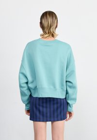 Sudadera extragrande de color azul claro con cuello redondo y dobladillo acanalado, combinada con una falda mini a rayas de color azul marino. Textura de tejido suave y acogedora.