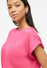 Camicetta rosa corta con maniche arrotolate, realizzata in tessuto morbido. Collo rotondo e vestibilità ampia, che mette in risalto un design casual e moderno.