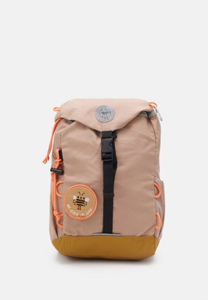 Brun og sennepsfarvet rygsæk med sort frontspænde, orange snore, netlomme på siden og rund bi-badge med teksten "Vær venlig i livet."