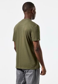 Tricou din bumbac verde măsliniu, cu mâneci scurte și gât rotund, având o textură netedă și o croială lejeră. Fără modele sau accente vizibile.