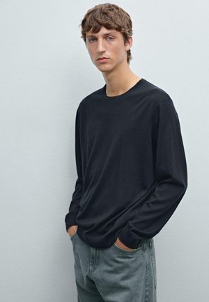 Black long-sleeve shirt in a soft fabric, featuring a crew neckline. Paired with light gray jeans, displayed against a plain background.