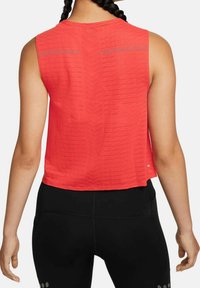 Punainen hihaton urheilupaita, jossa on teksturoitu kuvio, pyöreä pääntie ja rento istuvuus, yhdistettynä mustiin leggingsseihin, joissa on hopeisia pilkkuja.