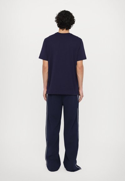 T-shirt navy a maniche corte con colletto rotondo, abbinato a pantaloni navy con strisce bianche sui lati. Tessuto morbido, vestibilità rilassata, design minimal.