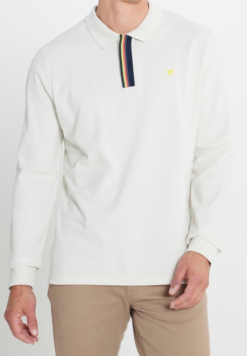 Camisa polo blanca de manga larga con un cuello a rayas multicolores y un pequeño logo amarillo en el pecho. Tejido suave y corte clásico.