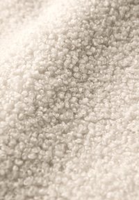 Tissu blanc texturé avec une surface en boucle et moelleuse. Le matériau semble doux et pelucheux, adapté aux vêtements ou accessoires confortables.