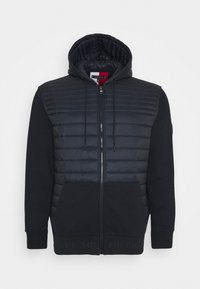 Czarna bluza z kapturem na zamek błyskawiczny z pikowanym przednim panelem, z kapturem na sznurki, przednimi kieszeniami i ściągaczami, wyeksponowana na białym tle.