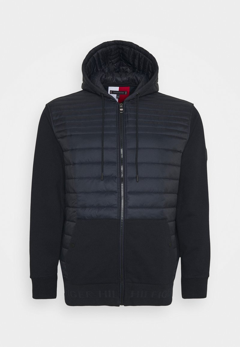 Czarna bluza z kapturem na zamek błyskawiczny z pikowanym przednim panelem, z kapturem na sznurki, przednimi kieszeniami i ściągaczami, wyeksponowana na białym tle.