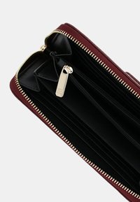 Portafoglio bordeaux con cerniera, esterno texturizzato, interno nero, molteplici slot per carte e tiretto della cerniera color oro.