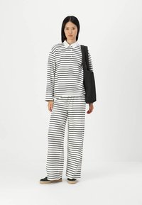 Black and white striped long-sleeve polo top paired with wide-leg striped pants; model holds a black tote bag; casual design and lightweight fabric.