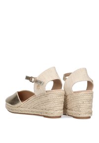 Cuñas de espadrille metálicas doradas con parte superior de yute beige y correa de tobillo. Presentan una suela de plataforma de 5 cm envuelta en cuerda. Textura suave.