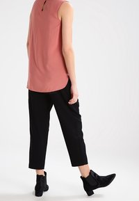 Haut sans manches rose avec une ouverture en forme de goutte d'eau dans le dos, assorti à un pantalon court noir et des bottines noires à bout pointu. Textures lisses partout.
