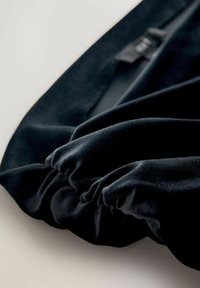 Sorte velourstof med en blød tekstur, der har samlet detalje langs kanten, hvilket skaber en glat, flydende form.