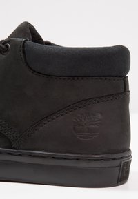 Musta nahkainen sneaker korkea malli, teksturoitu pinta, hienovaraiset ompeleet ja pyöreä logo sivussa. Sileä kumipohja.