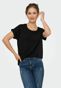 Sort kortærmet t-shirt i blødt stof med rund halsudskæring, parret med tætsiddende blå jeans med slidte detaljer.