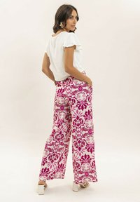 Haut blanc à volants à manches courtes associé à un pantalon large rose et blanc à motifs floraux avec des accents subtils.