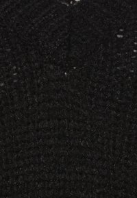 Černá pletená látka s texturovaným vzorem různé tloušťky. Měkká, vláknitá textura viditelná v detailním záběru.