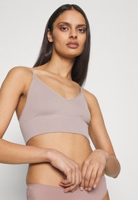 Brassière côtelée beige clair avec des fines bretelles ajustables et un col en V, dotée d'une bande élastique douce en bas pour le confort.