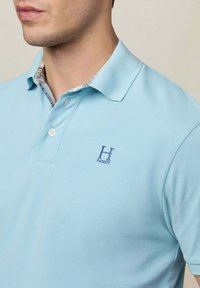 Polo shirt blu chiaro con un tessuto testurizzato; presenta un colletto con un rivestimento interno decorato e un logo ricamato sul petto.